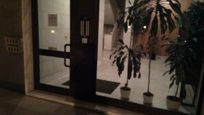 Entrada de hotel con puerta de cristal, plantas en macetas y suelo de baldosas.