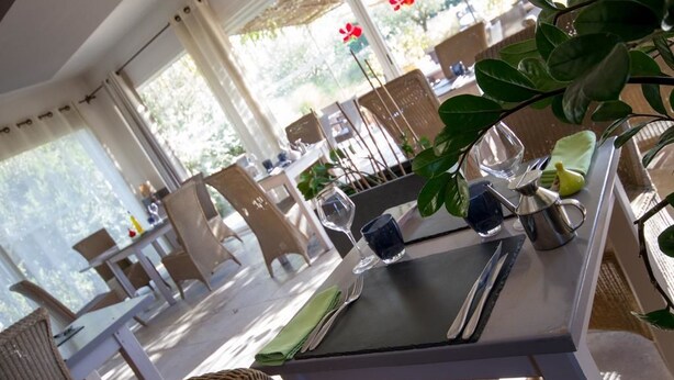 Comedor con mesas dispuestas para dos, con sillas de mimbre y vistas al exterior.