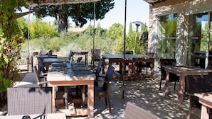 Un patio exterior con varias mesas y sillas, rodeado de follaje y una pérgola.