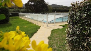 Piscina con cerramiento de vidrio, rodeada por un césped cuidado y setos.