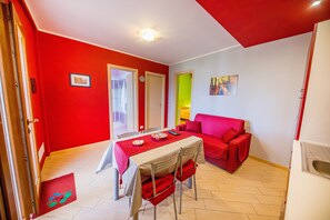 Un comedor con una mesa dispuesta para dos, un sofá rojo y un refrigerador blanco.
