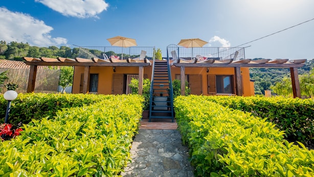 Ein Hotel mit einer zentralen Treppe, die zu einem Balkon mit Sonnenschirmen führt, umgeben von gepflegten Hecken.