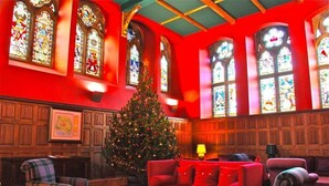 Una habitación cálidamente iluminada con un árbol de Navidad, muebles rojos y vidrieras.