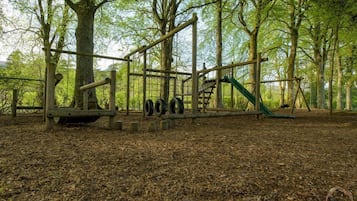 A playground with a slide, swings, and tire climbing equipment in a wooded area.