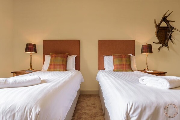 A hotel room with two beds, each with white linens and plaid pillows. There are bedside lamps and a wall-mounted deer antler decoration.