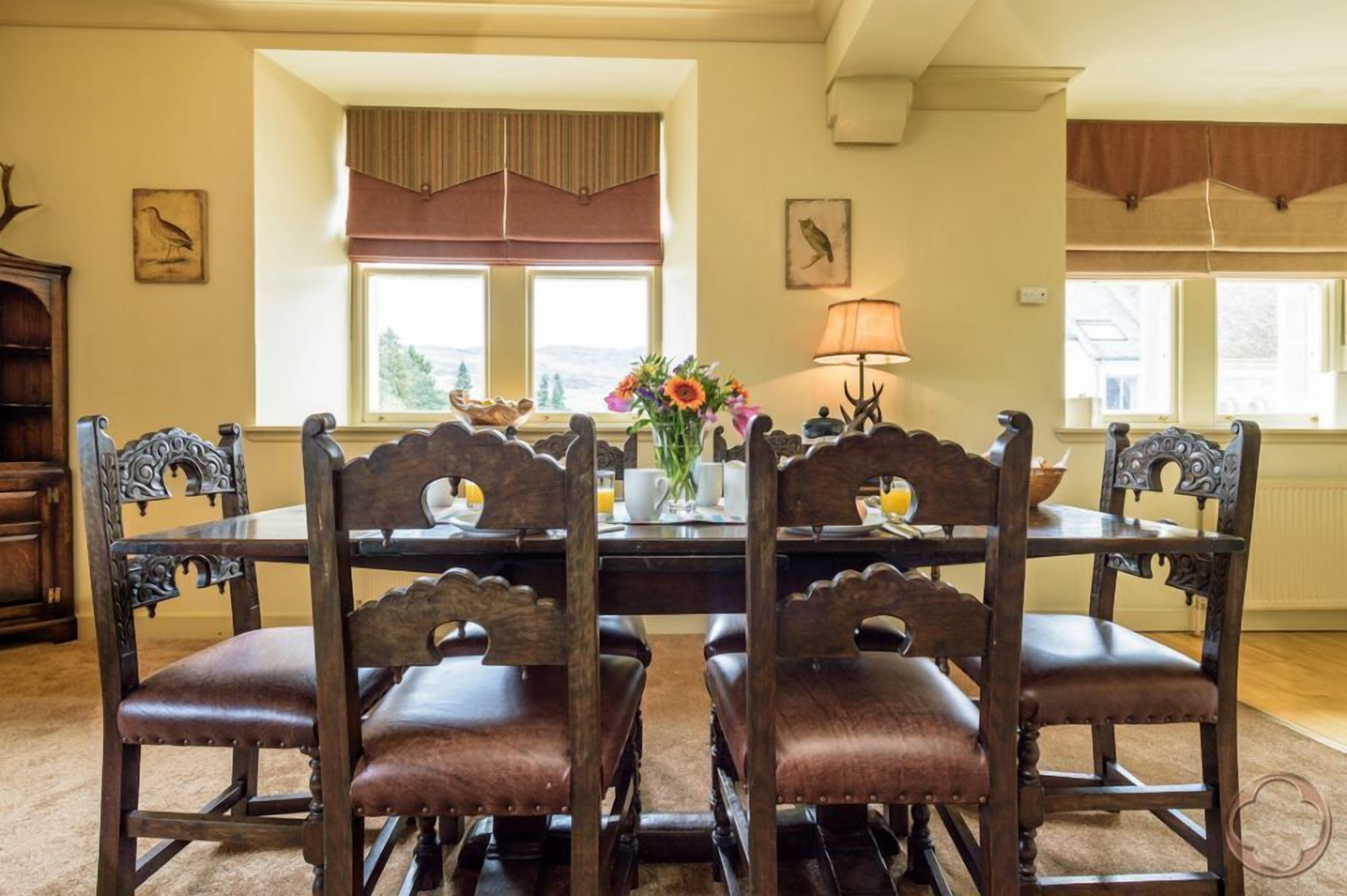 A dining area with a wooden table and chairs, a vase with flowers, and a lamp.
