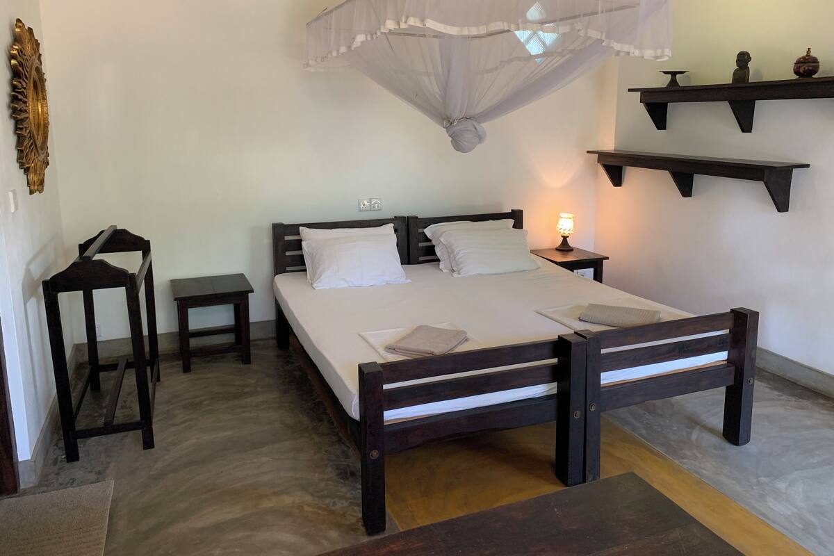 Um quarto bem organizado com uma cama, mesas de cabeceira, uma cadeira, mosquiteiro suspenso e prateleiras fixadas na parede.