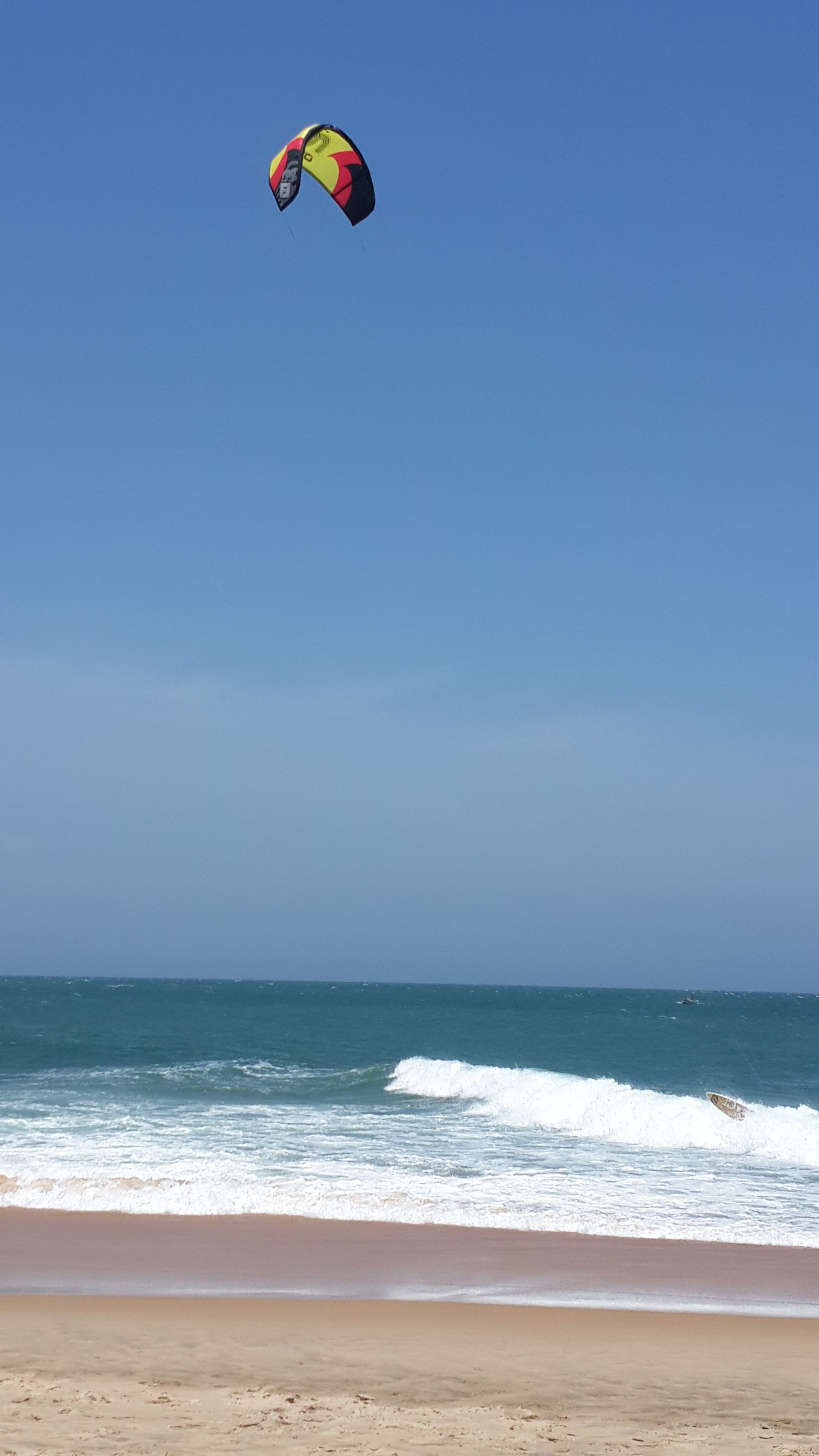 A beach with waves and a kite surfer in the air.