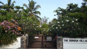 A gated entrance to The Danish Villa with a sign indicating air conditioning, satellite TV, and laundry service. - The Danish Villa (Arugam Bay)