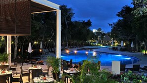 Un espace extérieur avec piscine, agrémenté de sièges et de tables, entouré d’arbres et bordé d’un bâtiment doté d’un toit en pente.