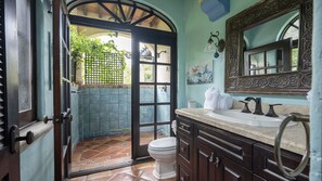 Une salle de bain avec un sol carrelé, des toilettes blanches, un lavabo doté d’un plan de travail en marbre et un miroir décoratif.