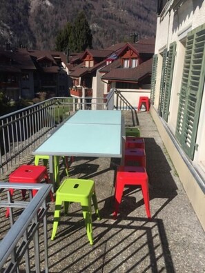 A terrace with a table and colorful stools, overlooking a mountain and residential buildings.