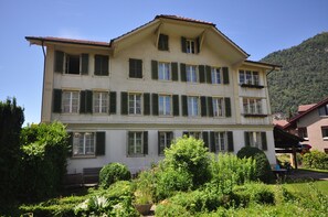 A two-story building with a balcony on the second floor, surrounded by lush greenery.