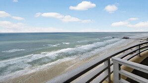 Blick auf den Strand vom Balkon mit Geländer, das Meer und ein Pier in der Ferne.