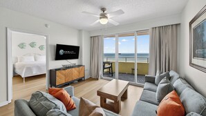 Ein modernes Hotelzimmer mit Balkon, einem Bett, einer Couch, einem Fernseher und einem Deckenventilator.