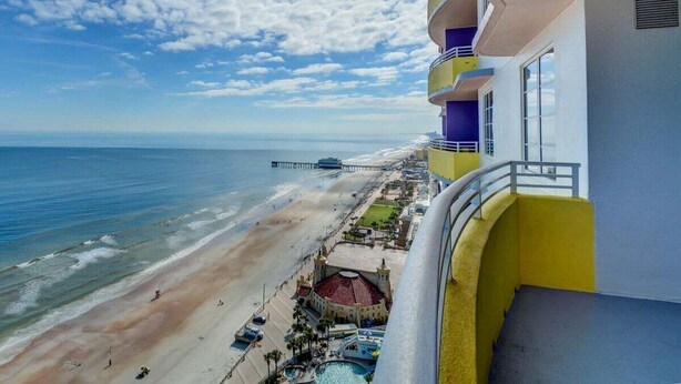 Ein Hotel mit Balkon, der auf einen Strand und den Ozean blickt, mit Pool und einem Steg im Hintergrund.