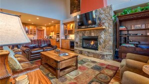 A spacious living area with a stone fireplace, leather sofas, and a television mounted on a stone wall. - Emmett's Overlook (Breckenridge)