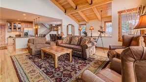 A spacious living area with a high ceiling, wooden beams, a large sofa, a coffee table, and a kitchen in the background. - Emmett's Overlook (Breckenridge)