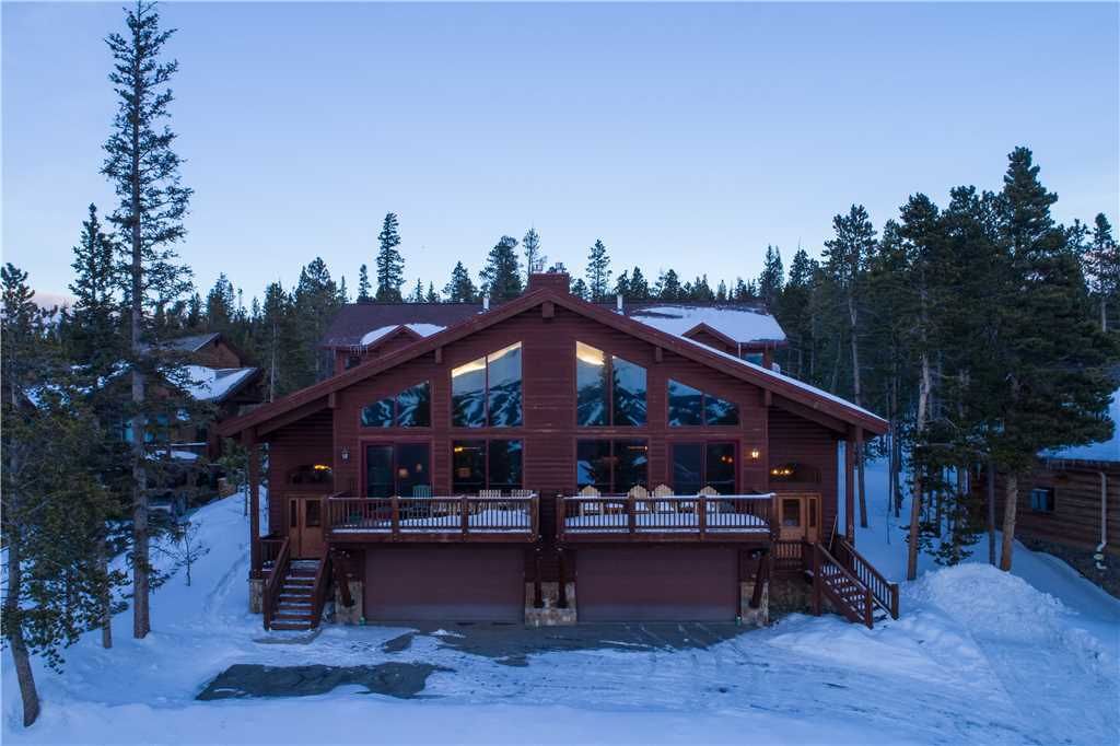 A large lodge with multiple windows and a balcony, surrounded by snow and trees.