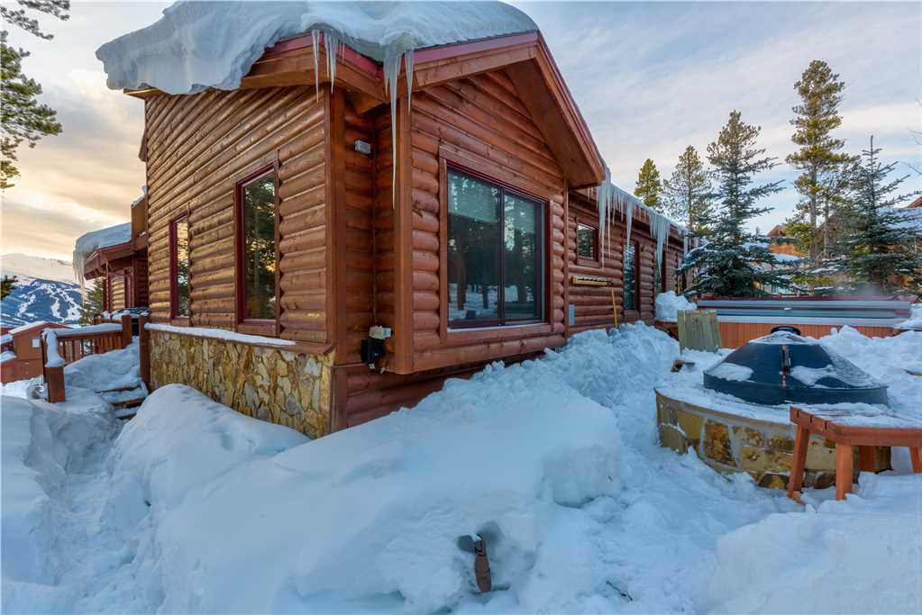 A log cabin with a snow-covered roof, windows, and a stone foundation.
