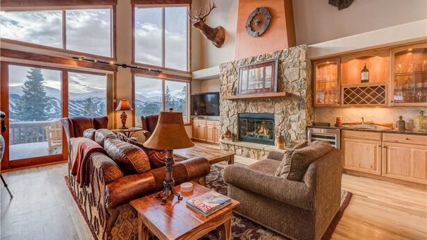 A spacious living area with a stone fireplace, leather sofas, and a large window overlooking a snowy landscape. - Emmett's Overlook (Breckenridge)