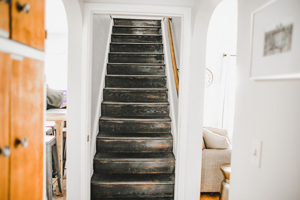 Eine Treppe führt zu einem Raum mit einer weißen Tür, einem Holztürrahmen und einem beigefarbenen Sofa.