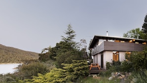 Ein modernes Haus mit einer Terrasse, umgeben von Bäumen und einem See.
