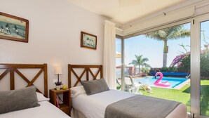 Ein Hotelzimmer mit zwei Betten, einem Nachttisch, einer Lampe und Blick auf einen Swimmingpool mit einem Flamingo-Schwimmpfad.