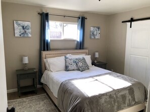 A bedroom with a bed, two nightstands, a window with curtains, and two wall-mounted floral paintings.