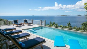 Zona de piscina con sillones de descanso y vista al mar.