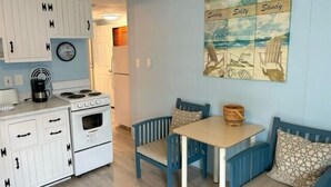 A compact kitchen with white cabinetry, a stove, and a dining area with blue chairs and a table. - Oceanfront condos with rare 2 night minimum rentals and linens included! (Ocean City)
