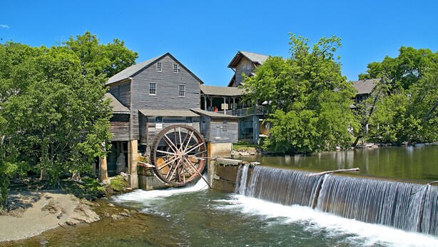 Un ancien moulin doté d’une grande roue à eau, de bâtiments en bois et bordé par une rivière.
