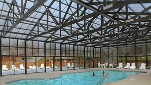 Une piscine intérieure dotée d’un toit en verre, entourée de chaises longues.
