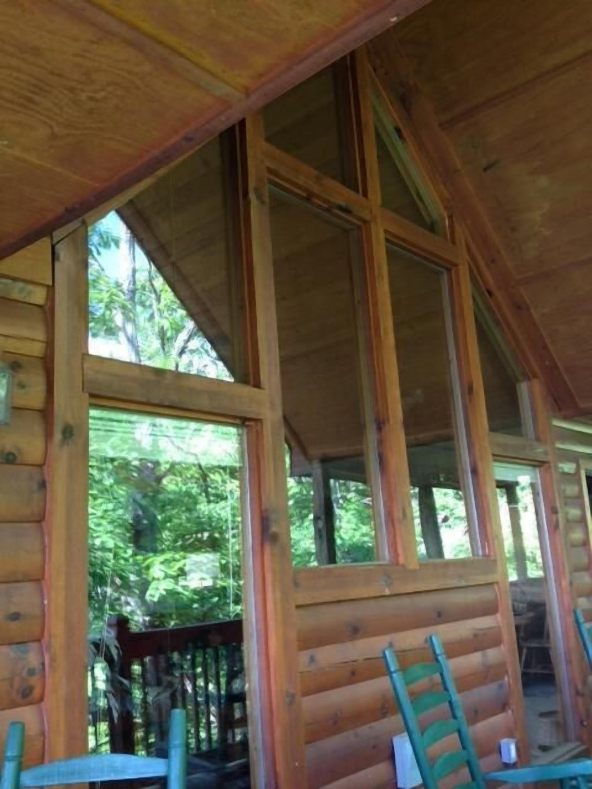 Une cabane en bois dotée de grandes fenêtres, d’une terrasse en bois et d’une échelle.