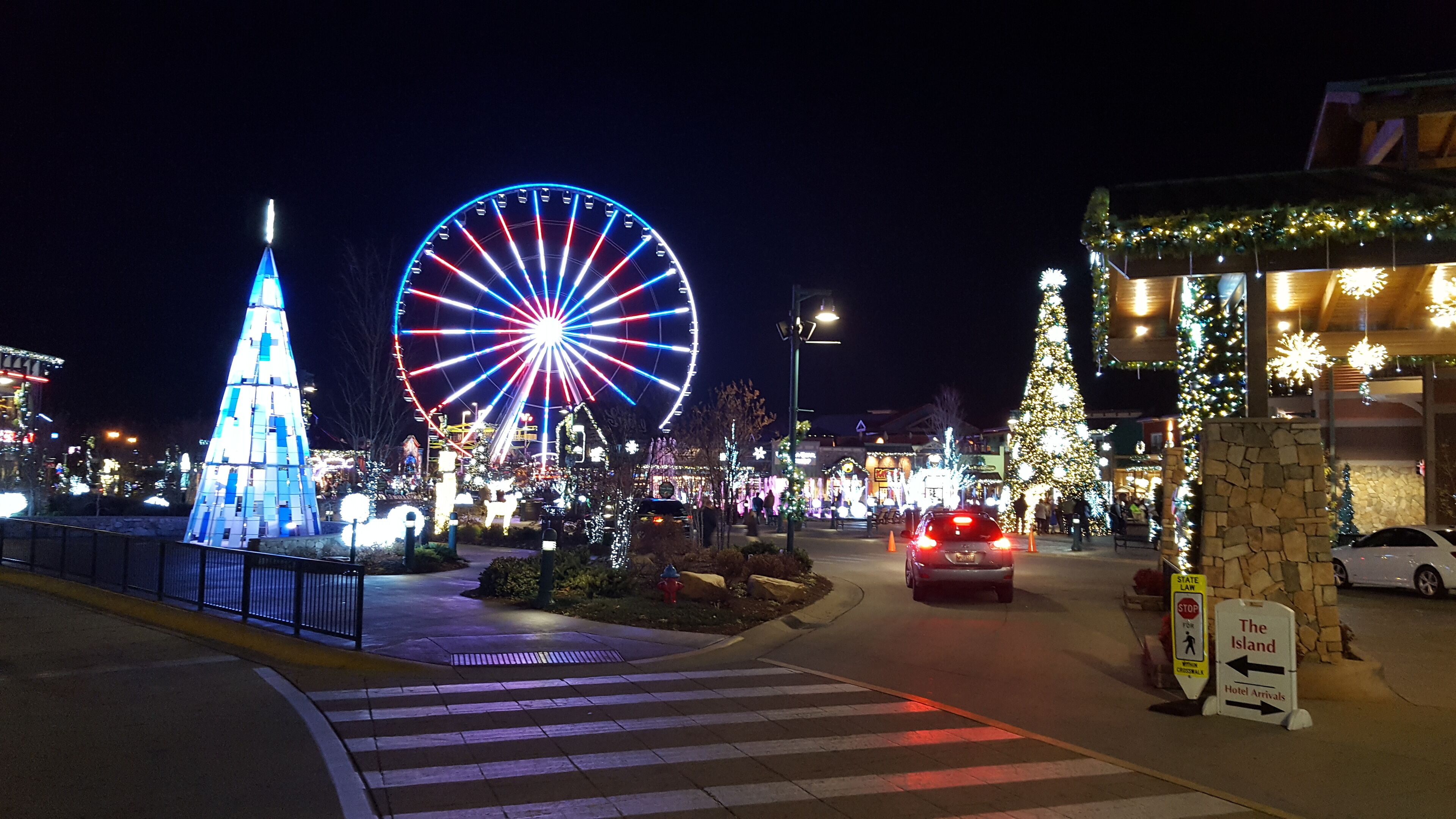 A brightly lit street with a Ferris wheel and a Christmas tree.