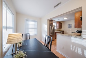 A modern kitchen with stainless steel appliances, a dining area with a black table and chairs, and a view of the living area through an open doorway. - Wrigley Rooftop Residence Next to Wrigley Field - Outdoor Patio - BBQ Grill (Chicago)