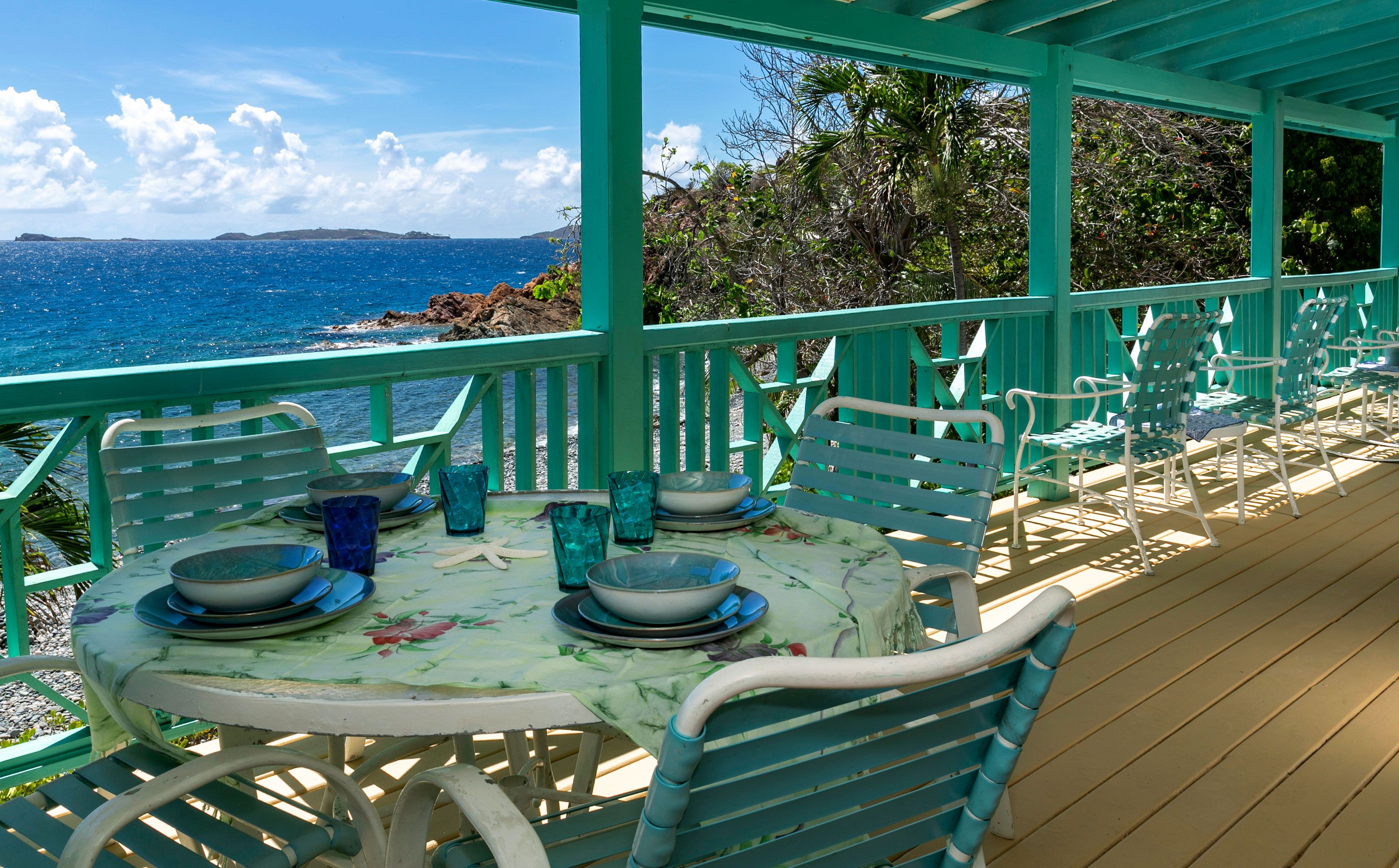 A covered outdoor dining area with a view of the sea and rocky coastline.