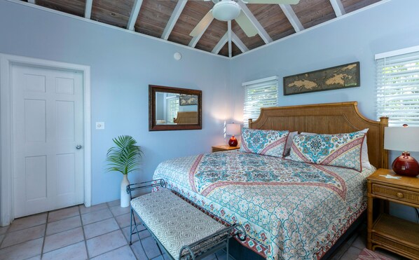 A bedroom with a bed, a nightstand, a lamp, a mirror, a door, and a ceiling fan. - Sunset Beach: Beachfront Villa! Pool! Hot Tub! (St. John)