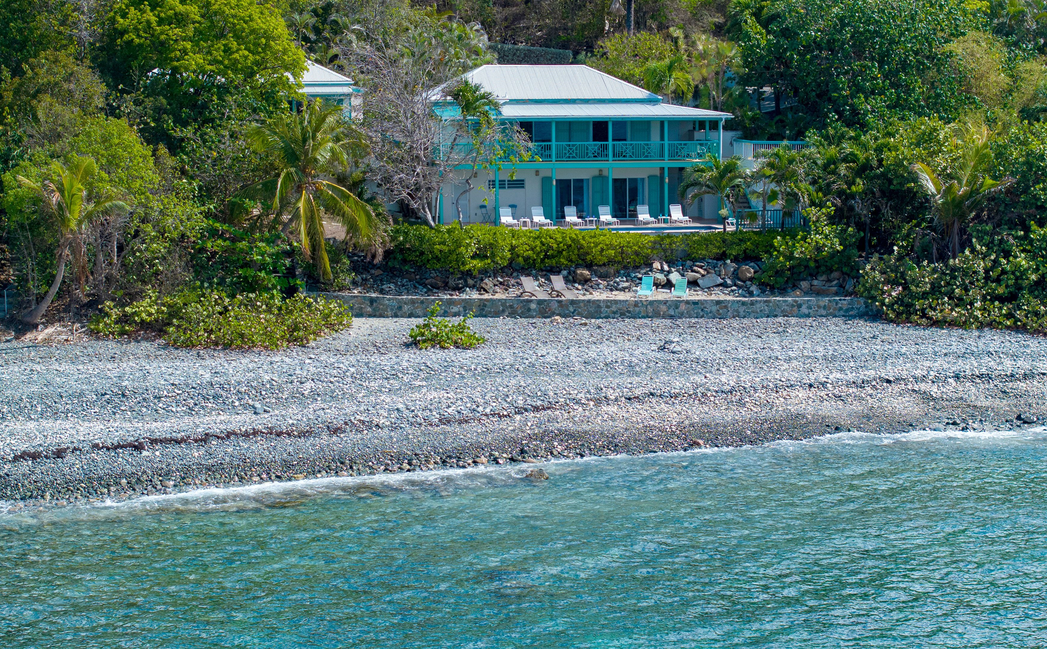 A beachfront property with a large building, a pebble beach, and a clear view of the ocean.