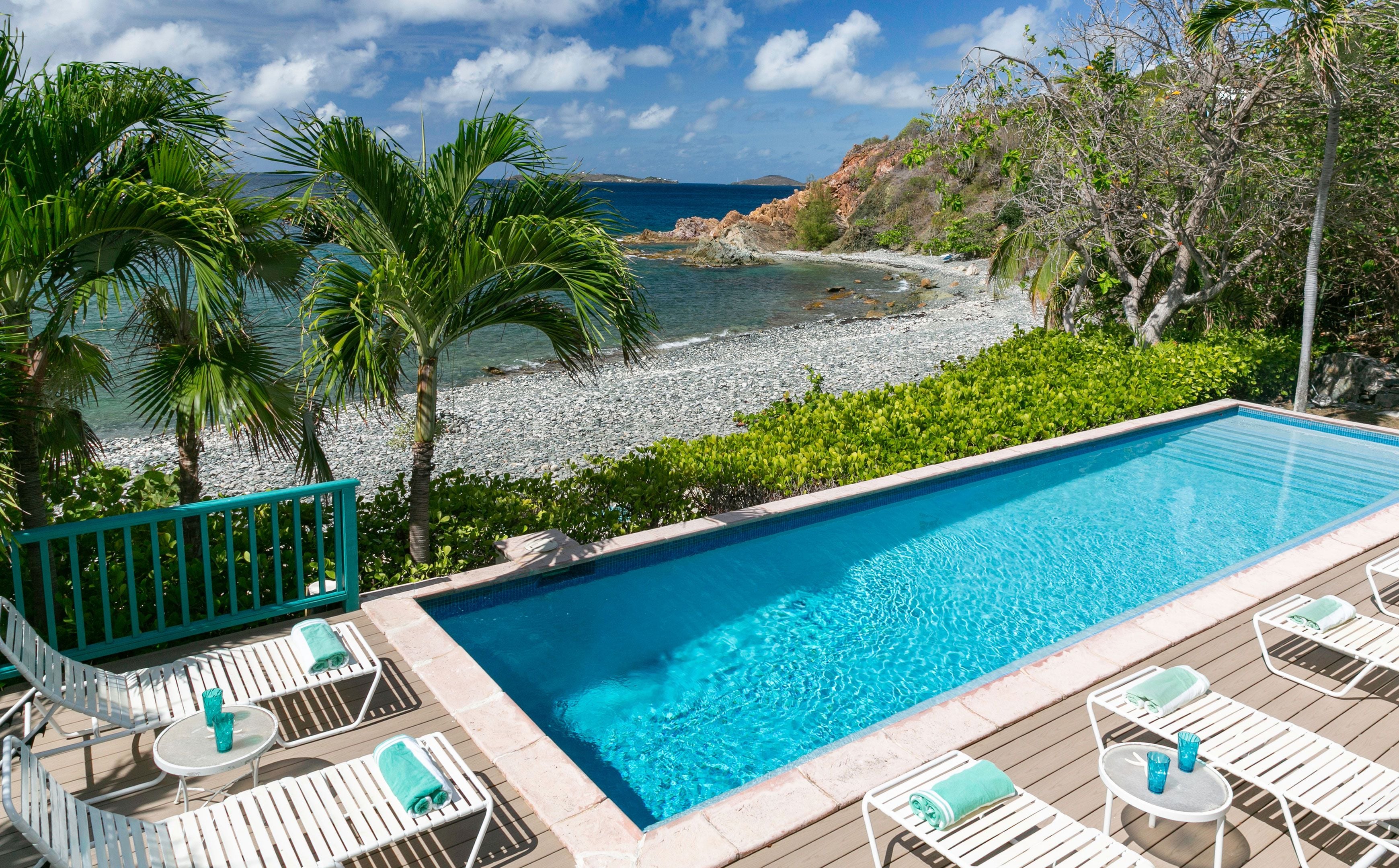 A clear blue pool with white lounge chairs and a view of the beach and ocean.