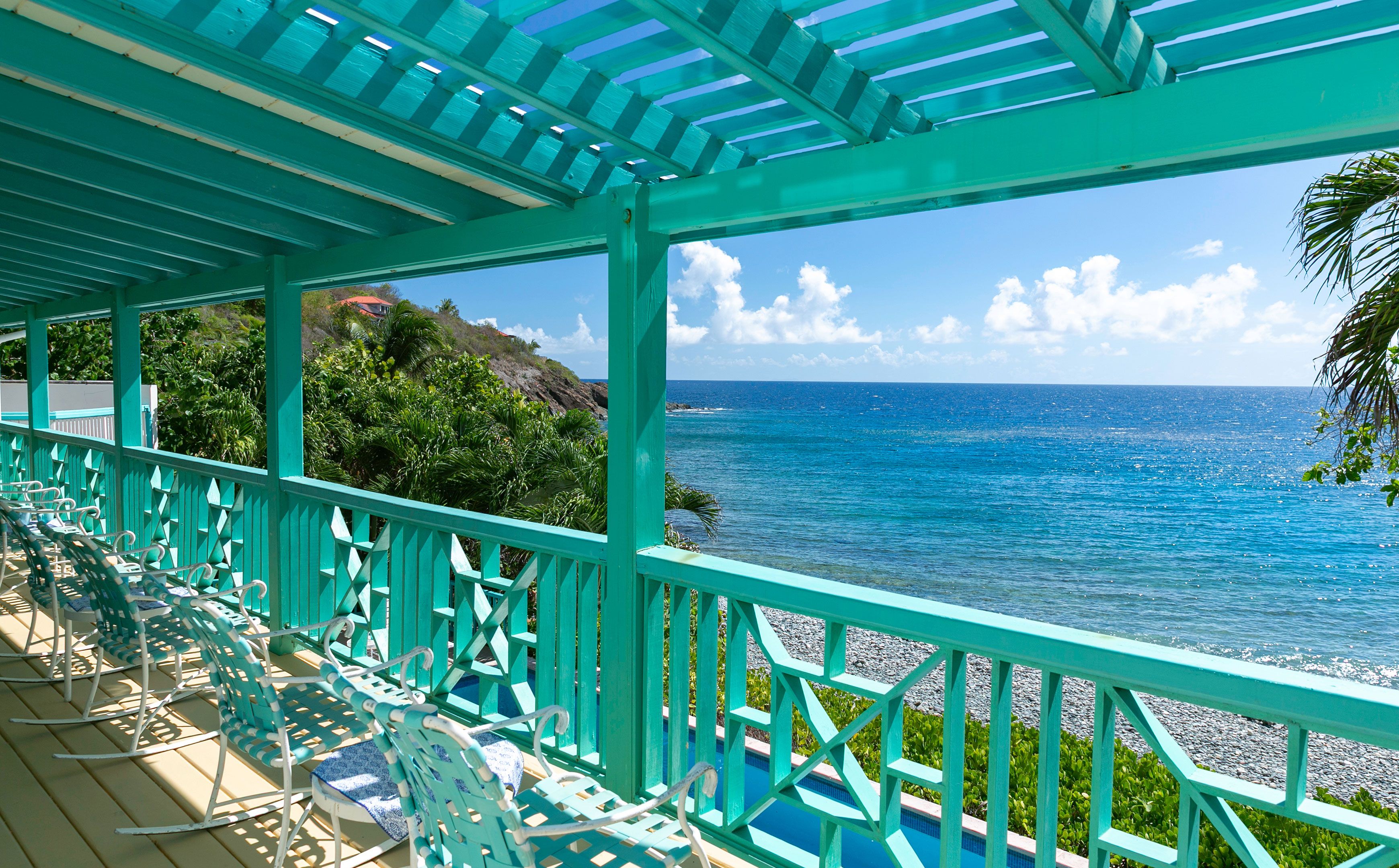 Ein überdachter Außenbereich zum Sitzen mit Stühlen und Blick aufs Meer.