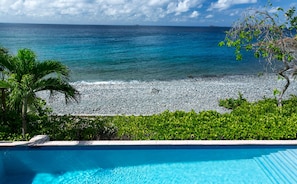 A clear blue pool with a view of a pebbled beach and the ocean. - Sunset Beach: Beachfront Villa! Pool! Hot Tub! (St. John)