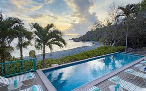 A swimming pool with lounge chairs and a view of the sea. - Sunset Beach: Beachfront Villa! Pool! Hot Tub! (St. John)