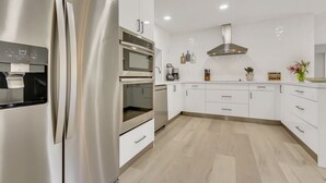 A modern kitchen with stainless steel appliances, white cabinetry, and a wooden floor. - WatersEdge: Lakefront Fishing-Saltwater Pool-GameRoom (Weston)