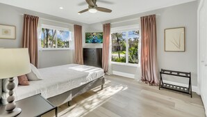 A bedroom with a bed, a ceiling fan, a window with curtains, a bedside table with a lamp, and a bench by the window. - WatersEdge: Lakefront Fishing-Saltwater Pool-GameRoom (Weston)