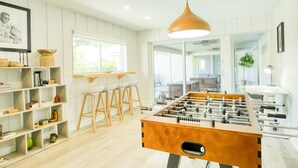 A modern kitchen with a foosball table, wooden bar stools, and a large window. - WatersEdge: Lakefront Fishing-Saltwater Pool-GameRoom (Weston)