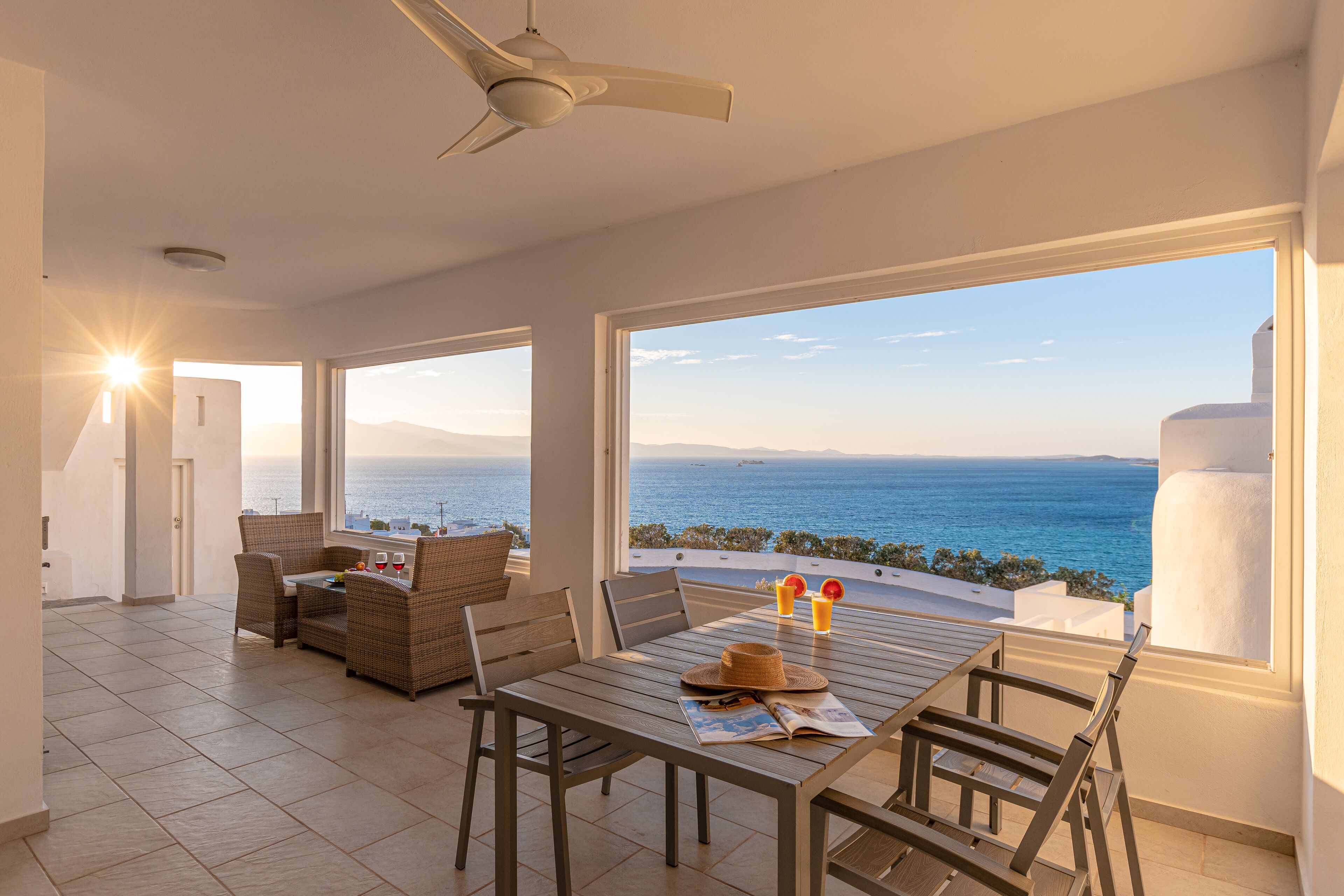 A spacious balcony with a view of the sea, furnished with wicker chairs and a table, and a ceiling fan.
