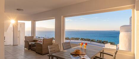 A spacious balcony with a view of the sea, furnished with wicker chairs and a table, and a ceiling fan.