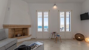 Een woonkamer met een open haard, een bank, een salontafel met een tijdschrift, een bijzettafeltje met een lamp en een aan de muur bevestigde televisie.