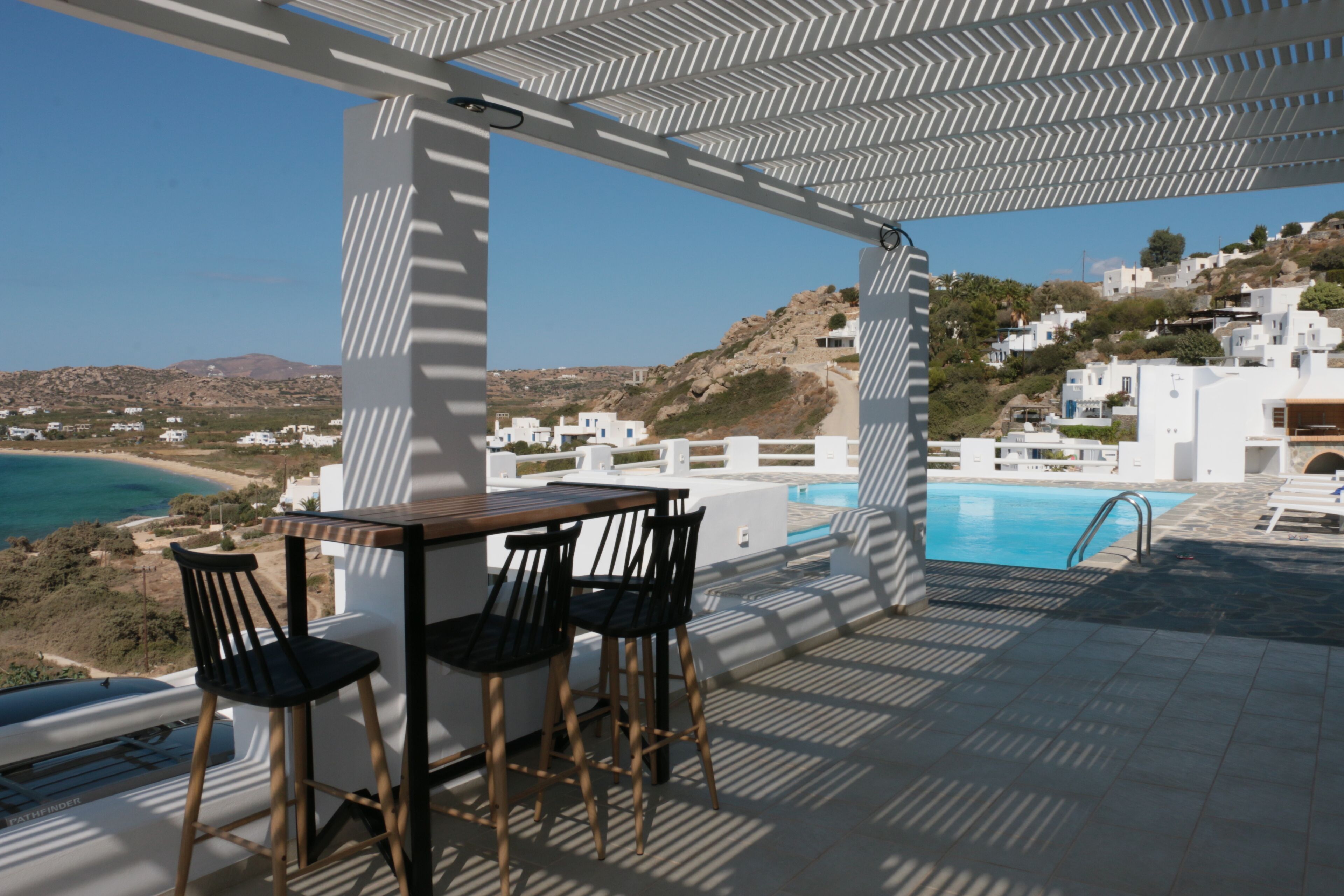 Una terraza al aire libre con piscina, edificios blancos y vistas a la costa.